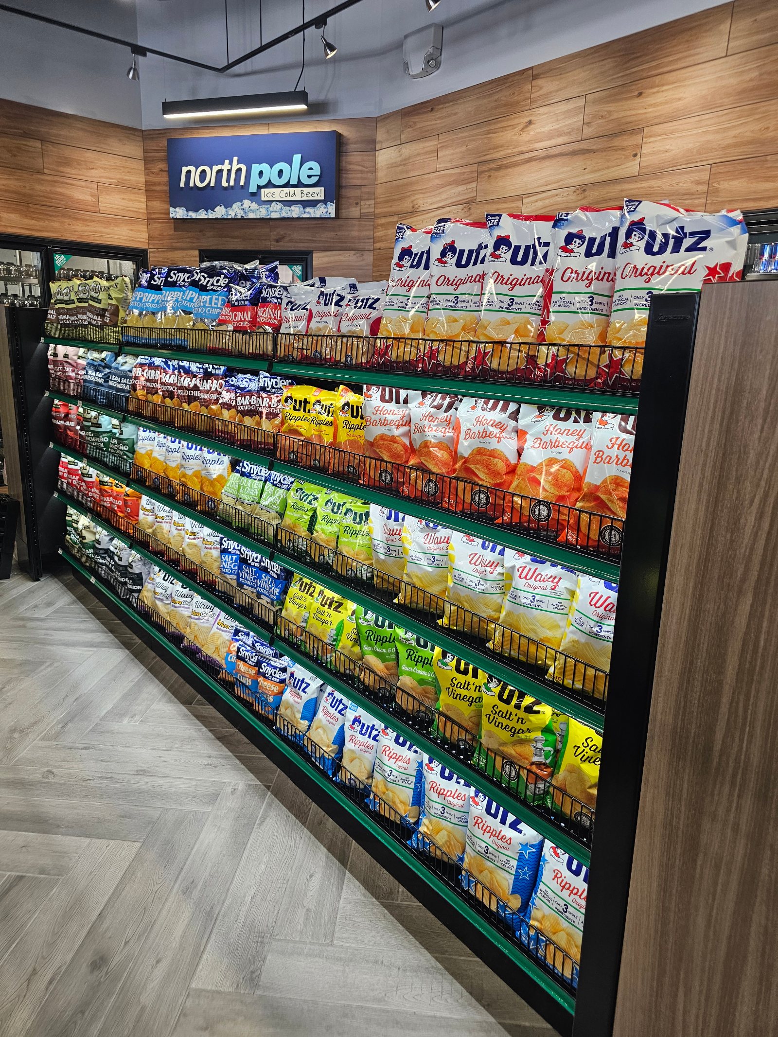 A long snack gondola in a modern convenience store, faced front and fully stocked five shelves deep with bagged chips